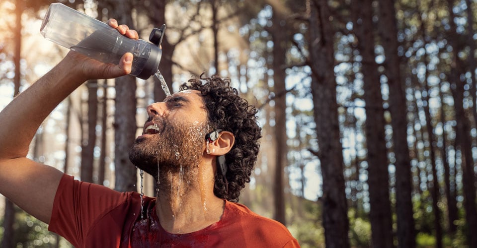 Sportler gießt Wasser über wasserdichte Open-Ear-Kopfhörer