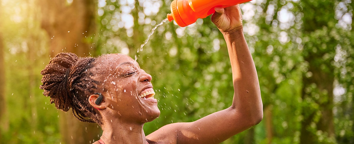 Frau kühlt sich ab, indem sie sich Wasser über den Kopf gießt, während sie Philips Sportkopfhörer im Freien trägt