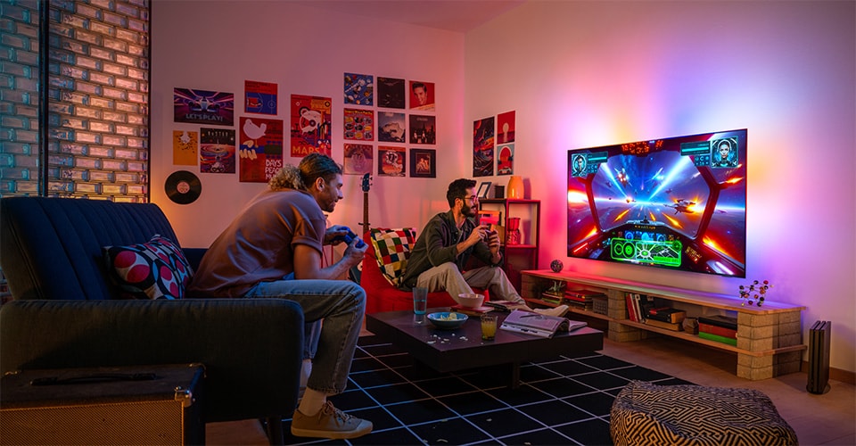 Deux personnes jouent avec enthousiasme à un jeu vidéo sur le thème de l'espace dans un salon confortable et coloré