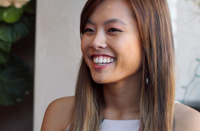 Eine junge Frau lächelt in die Kamera an und zeigt dabei ihre strahlend weißen Zähne.