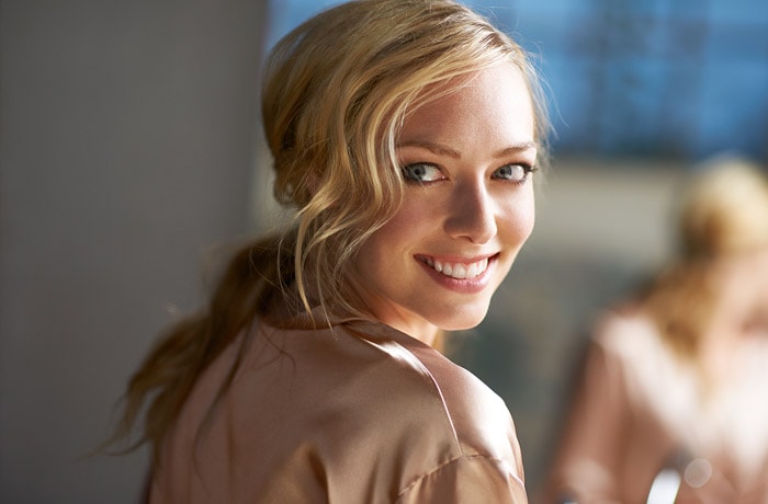 Eine junge Frau wendet sich der Kamera zu und blickt zur Seite. Sie lächelt und zeigt ihre strahlend weißen Zähne.