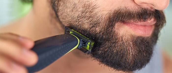 Nahaufnahme eines Mannes mit braunen Augen, der seinen dunklen Bart mit dem Philips OneBlade rasiert und trimmt